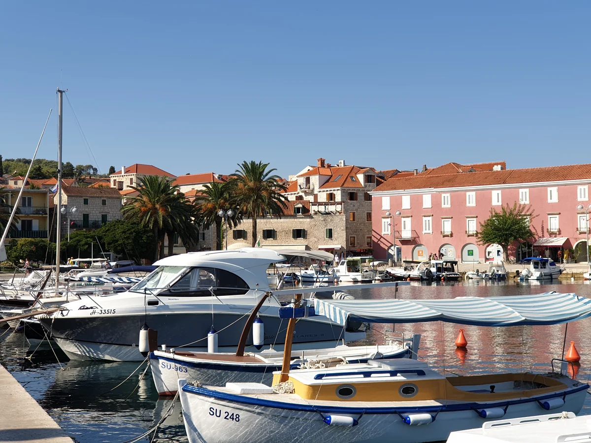 Small boats moored in Supetar harbour on Brač, with palm trees and the pink waterfront houses behind
